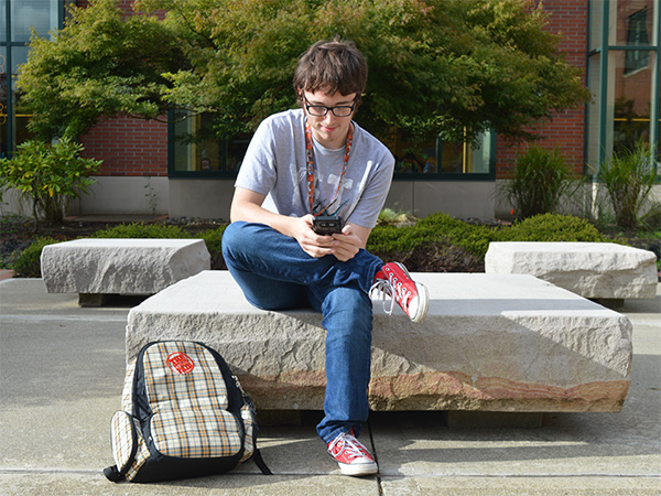 student sitting outside campus center browsing mobile phone