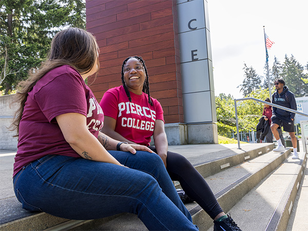 two students in pierce college shirts sitting outdoors on stairs