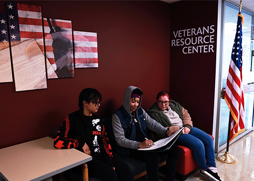 three students sit looking over papers outside the military and veterans resource center