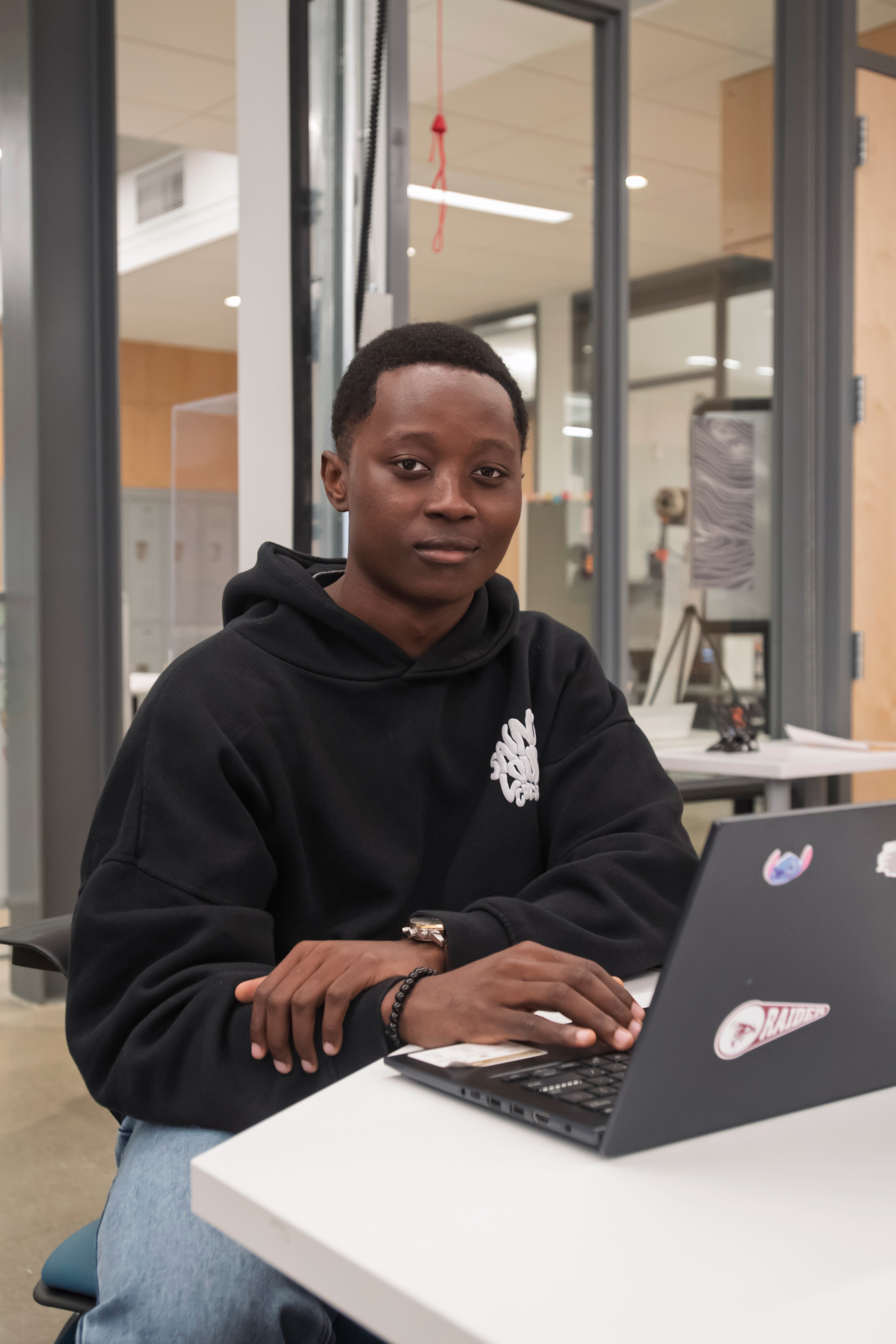 Believe Biduaya, Pierce College Student, wearing dark sweatshirt sits studying at with his laptop at a table in front of the Fabrication Lab in the Johnson Science Building