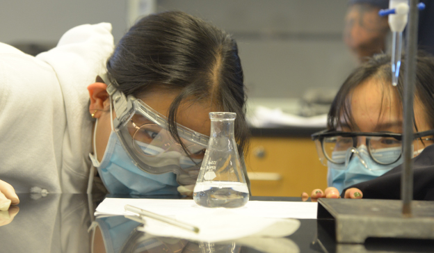 Two students examining a beaker during a chemistry lab experiment.