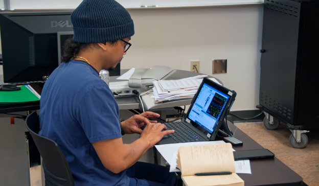 student in scrubs entering data into laptop